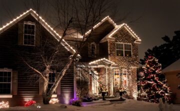 residential house with custom design of holiday lights lining roof and wrapped around a shrub in front yard