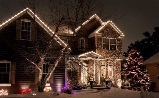 residential house with custom design of holiday lights lining roof and wrapped around a shrub in front yard