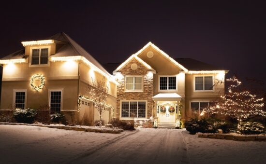Two story house in Eagan, Minnesota with white lights along roof line, in two small trees, a wreath and garland.