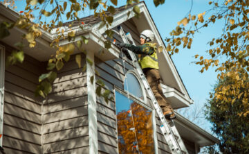 technician on ladder installing lights on roofline of residential house