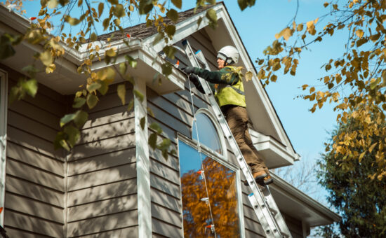 technician on ladder installing lights on roofline of residential house
