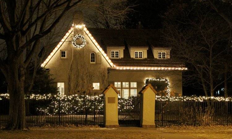 White Christmas lights on roofline, wreath, and hedges